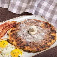 "First Watch Cinnamon Chip Pancakes with powdered sugar, eggs, and bacon – 2025 menu"